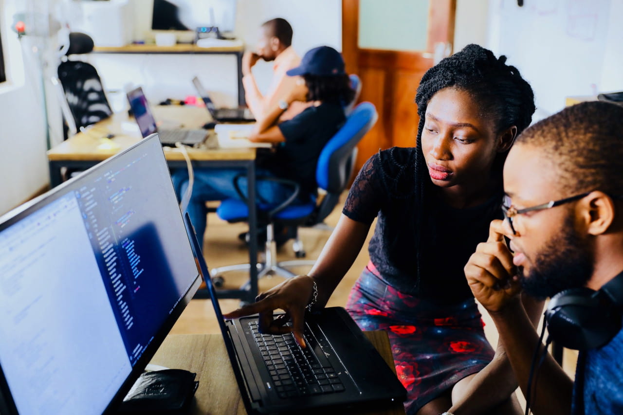 Two people staring at a laptop screen with one of them pointing at something on the screen